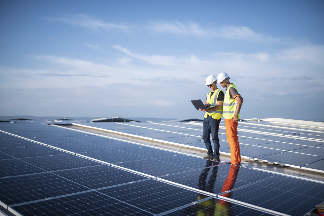 Team of engineers using technology while installing solar panels on a roof of warehouse.